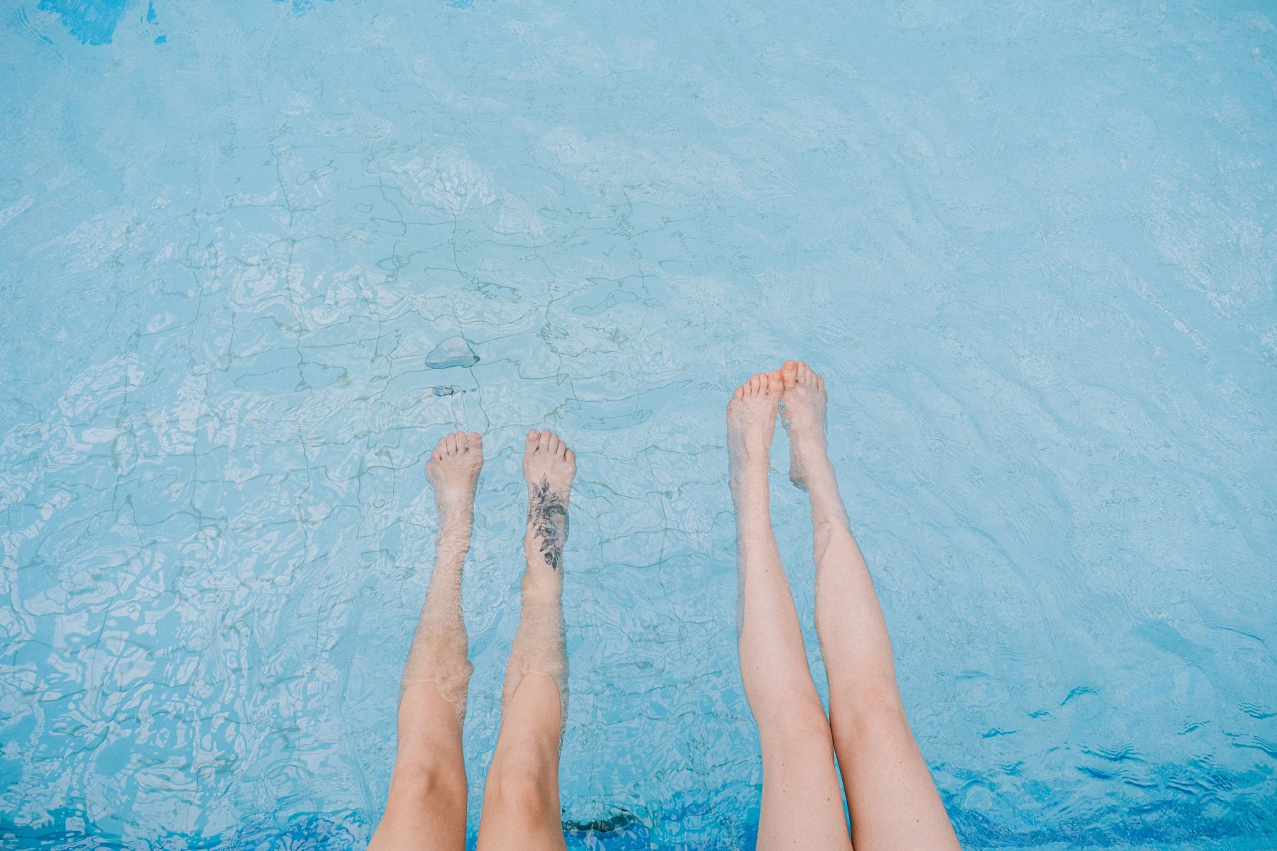 Two people dip their feet in a swimming pool
