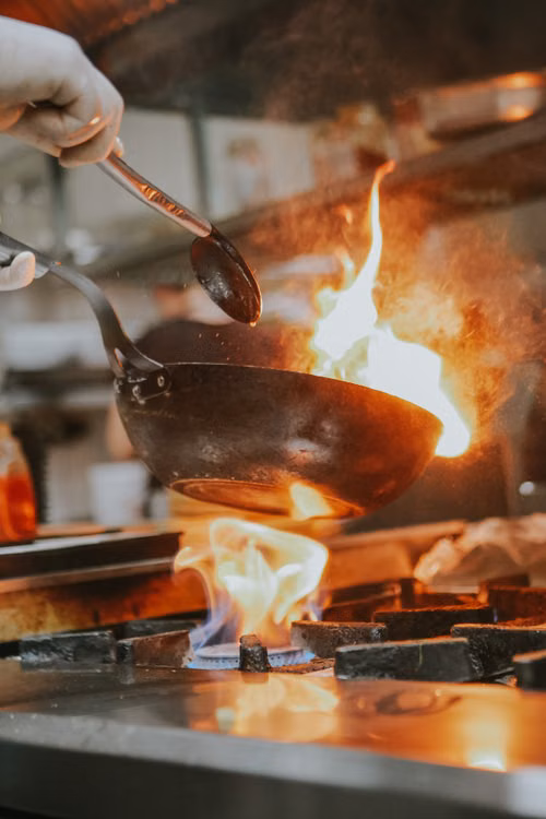 A cook handling a flaming pan in a restaurant kitchen