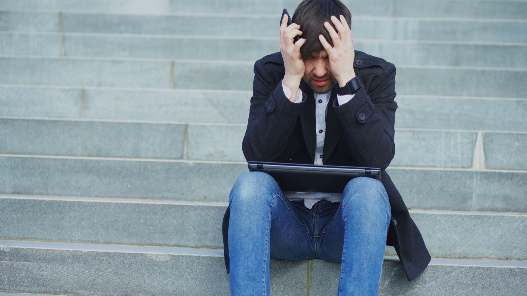 A frustrated person trying to work on a laptop outdoors