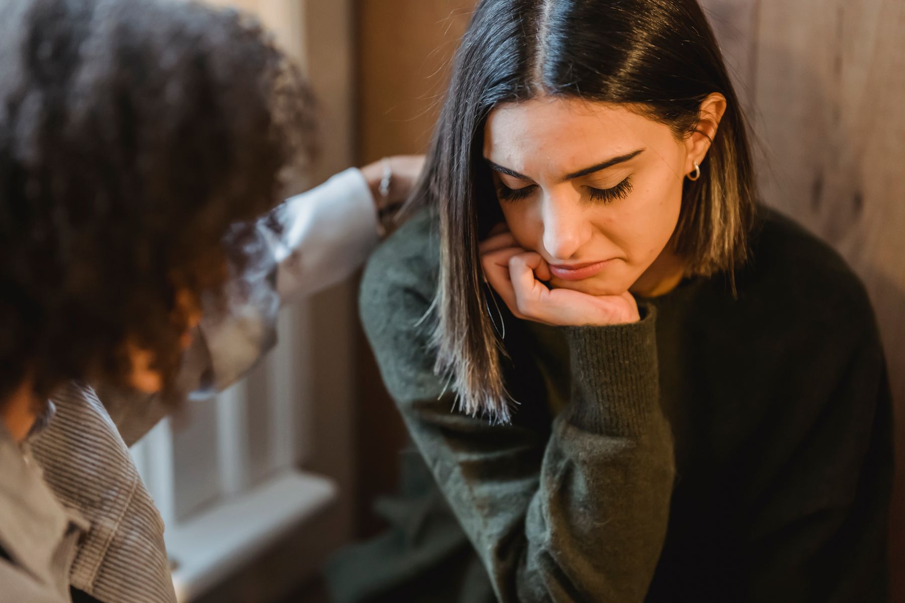 One friend gently comforting another with a hand on her shoulder