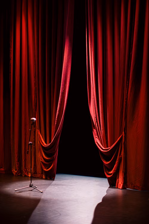 A theater stage with red curtains and a microphone in a spotlight