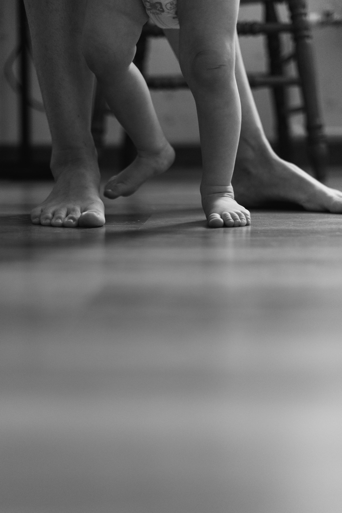A child taking first steps with an adult nearby